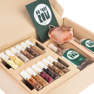 May include: A brown cardboard box filled with a DIY rum kit. The kit includes a bottle of rum, a strainer, and several small glass vials filled with different ingredients. The box also includes a green card with the text "Do Your Rum".