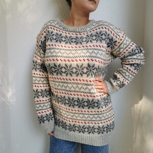 May include: A gray, white, and red patterned sweater with a crew neck. The sweater has a snowflake design.