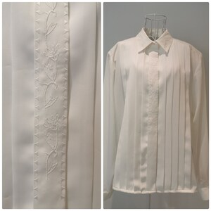 May include: A white long-sleeve button-down shirt with a pleated front and a floral embroidery detail down the center front.