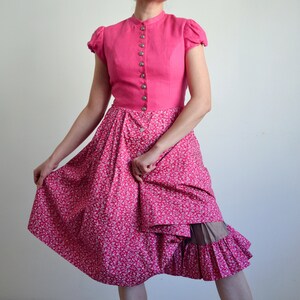 May include: A pink dress with a white floral print and a ruffled hem. The dress has a fitted bodice with a button-up front and short sleeves.
