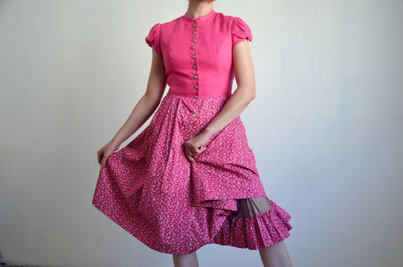 May include: A pink dress with a white floral print and a ruffled hem. The dress has a fitted bodice with a button-up front and short sleeves.