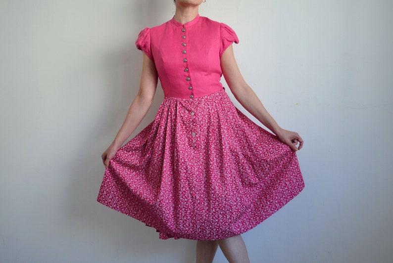 May include: A pink dress with a white floral print and a button-up bodice. The dress has short sleeves and a full skirt.