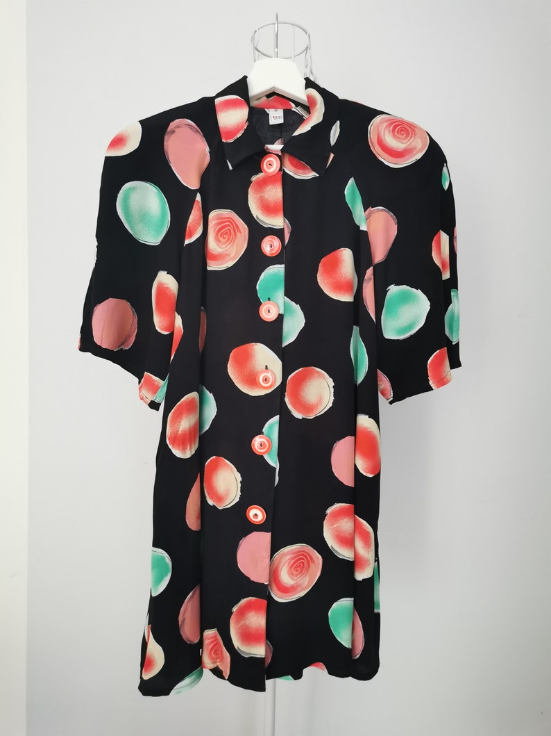 May include: A black button-up dress with a short sleeve and a colorful abstract print of red, pink, and green circles.