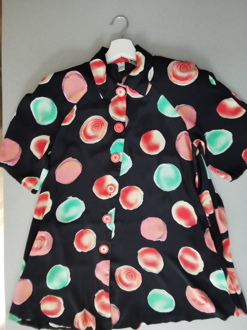 May include: A black button-up shirt with a short sleeve and a colorful abstract print of circles and swirls.