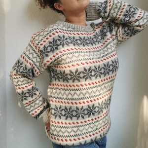 May include: A white, gray, and red patterned sweater with a crew neck. The sweater has a snowflake design.