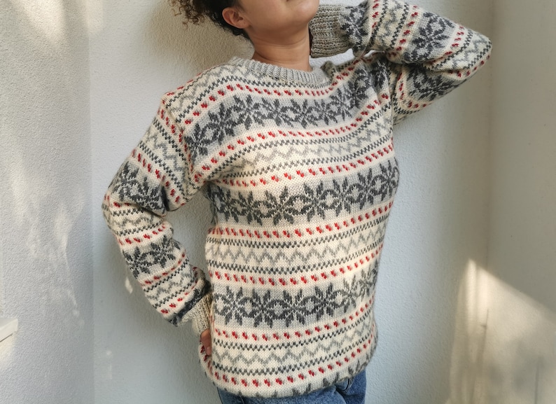 May include: A white, gray, and red patterned sweater with a crew neck. The sweater has a snowflake design.