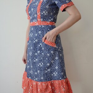 May include: A blue and white floral dress with a red trim. The dress has a square neckline, short sleeves, and a ruffled hem.