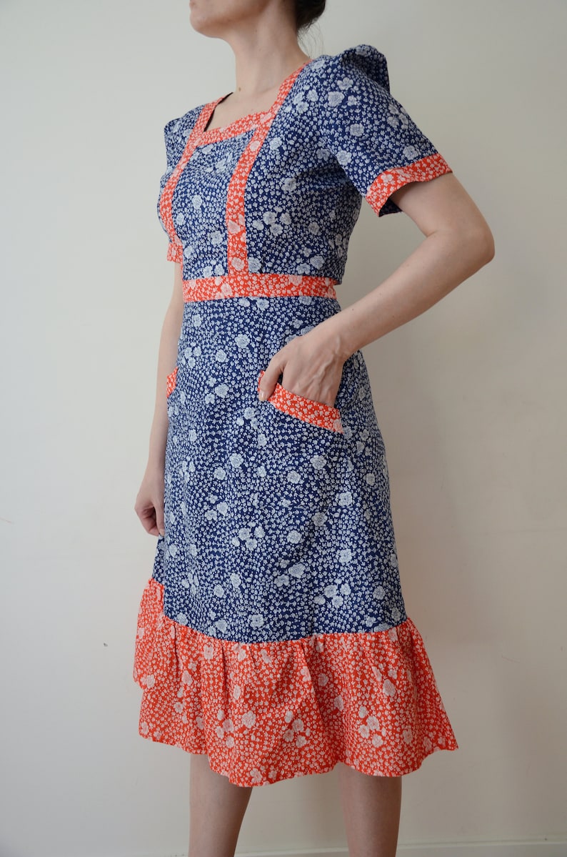 May include: A blue and white floral dress with a red trim. The dress has a square neckline, short sleeves, and a ruffled hem.