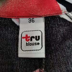 May include: A white tag with black trim and the text "tru blouse" in red and black. The tag also has the number "36" printed on it.