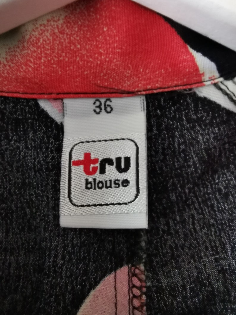 May include: A white tag with black trim and the text "tru blouse" in red and black. The tag also has the number "36" printed on it.