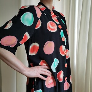 May include: A black button-up shirt with a short sleeve and a colorful abstract print of circles and swirls. The shirt has orange buttons.