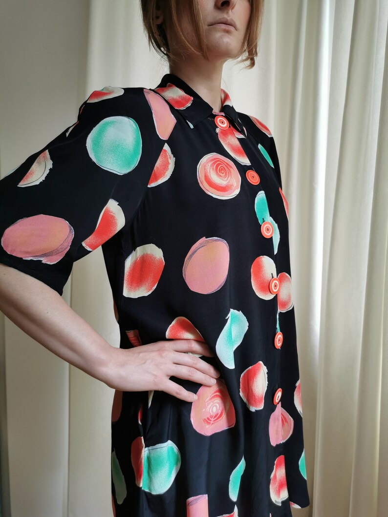 May include: A black button-up shirt with a short sleeve and a colorful abstract print of circles and swirls. The shirt has orange buttons.