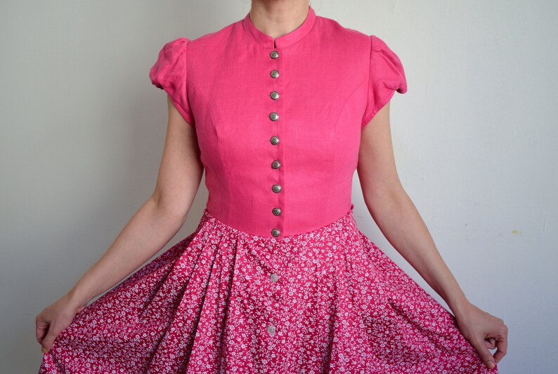 May include: A pink dress with a white floral print skirt and a solid pink bodice with a button-up front.