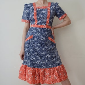 May include: A blue and white floral dress with a red trim. The dress has a square neckline, short sleeves, and a ruffled hem.