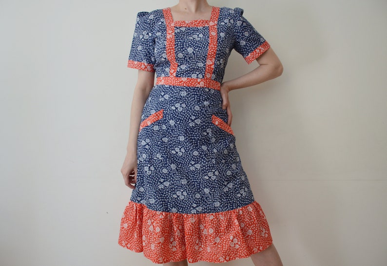 May include: A blue and white floral dress with a red trim. The dress has a square neckline, short sleeves, and a ruffled hem.