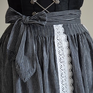 May include: A black and white striped skirt with a white lace trim and a matching bow. The skirt is gathered at the waist and has a full, flowing silhouette.
