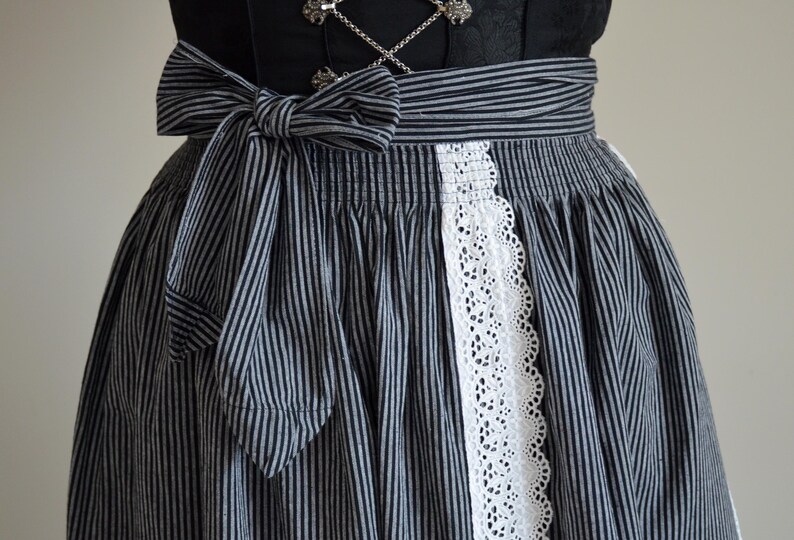 May include: A black and white striped skirt with a white lace trim and a matching bow. The skirt is gathered at the waist and has a full, flowing silhouette.
