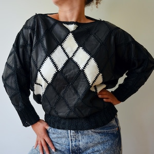 May include: Black and white diamond-patterned sweater. The long-sleeved top features a patchwork design with a black knit collar, cuffs, and waistband. The sweater has a boat neck and a relaxed fit, suitable for casual wear.