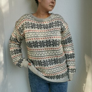 May include: A white, gray, and red patterned sweater with a crew neck. The sweater has a snowflake design.