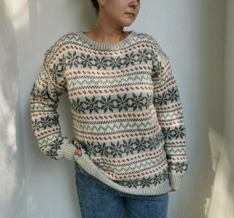 May include: A white, gray, and red patterned sweater with a crew neck. The sweater has a snowflake design.