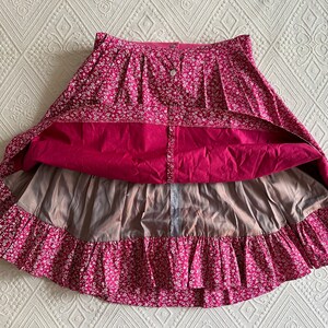 May include: A pink and white floral skirt with a ruffled hem and a button closure. The skirt has a lining and is made of a lightweight fabric.