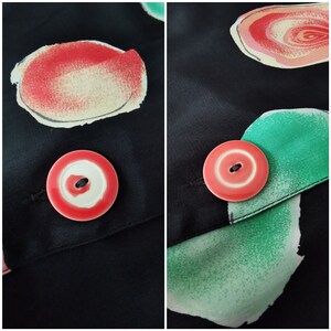 May include: A close-up of a black fabric with a pink button. The button has a white center and a black buttonhole. The fabric has a green and pink abstract design.