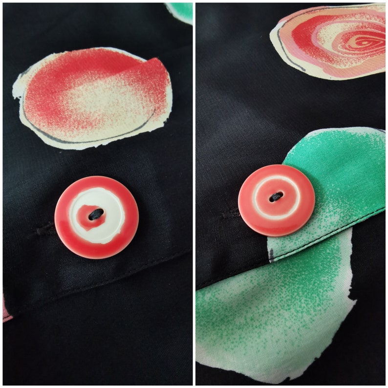 May include: A close-up of a black fabric with a pink button. The button has a white center and a black buttonhole. The fabric has a green and pink abstract design.