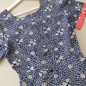 May include: A blue and white floral print short-sleeved dress with red trim on the sleeves and neckline. The dress has a button-up front.