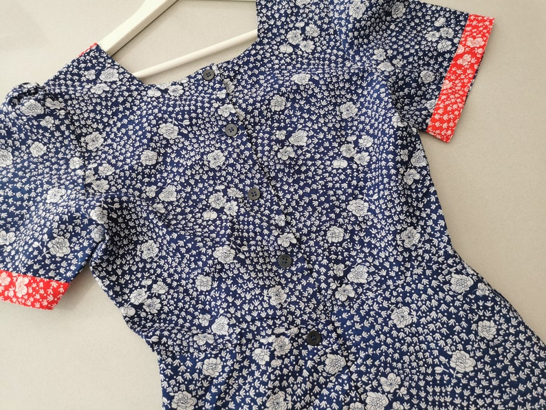 May include: A blue and white floral print short-sleeved dress with red trim on the sleeves and neckline. The dress has a button-up front.