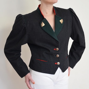 May include: A dark gray jacket with a red and green collar and trim. The jacket has three buttons and decorative gold accents on the collar. The sleeves are slightly puffed at the shoulders. The jacket is paired with white pants.