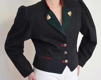 May include: A dark grey jacket with a red and green collar and trim. The jacket has three buttons and decorative gold accents on the collar. The sleeves are slightly puffed at the shoulders. The jacket is paired with white trousers.