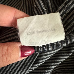 May include: A white fabric tag with black text that reads "100% Baumwolle" on a black and white striped fabric.