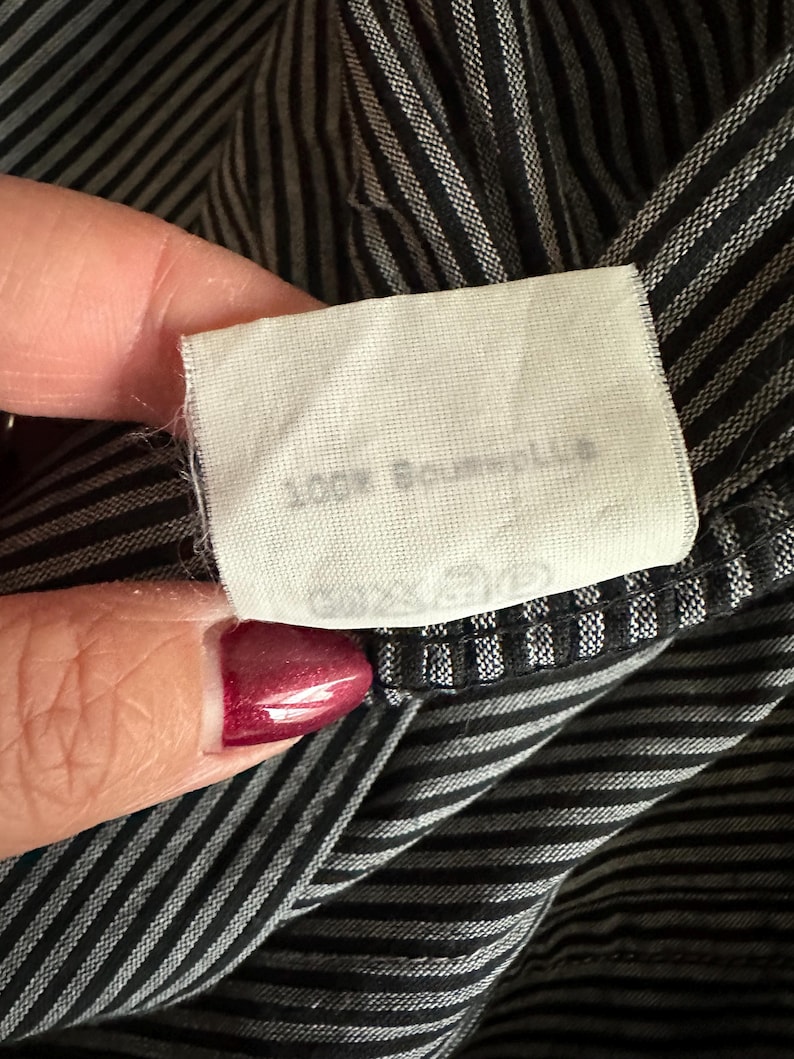 May include: A white fabric tag with black text that reads "100% Baumwolle" on a black and white striped fabric.