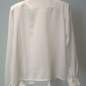 May include: A white long-sleeved button-up shirt with a collar and a small embroidered design on the collar.