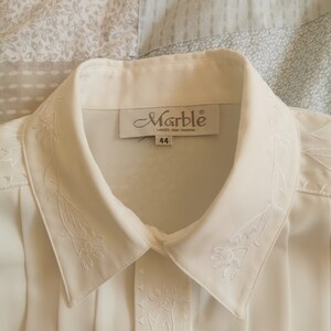 May include: White collared blouse with embroidered floral details. The blouse has a label that reads "Marble Ladies High Fashion" and "44".