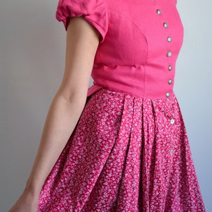 May include: A pink dress with a white floral print. The dress has a fitted bodice with a high neckline and short puffed sleeves. The skirt is full and gathered at the waist.