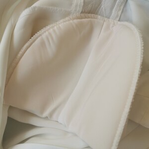 May include: Close-up of the inside of a white garment, showing the seam and lining. The fabric is soft and smooth.