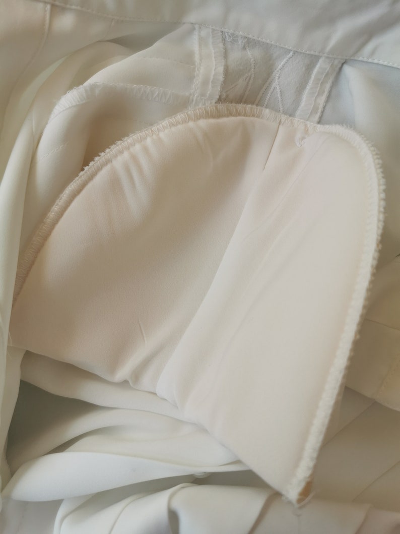 May include: Close-up of the inside of a white garment, showing the seam and lining. The fabric is soft and smooth.
