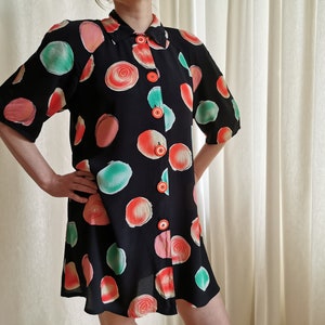 May include: A black short-sleeved button-up dress with a colorful abstract print of large circles in shades of red, pink, and green. The dress has a collared neckline and a button-up front.