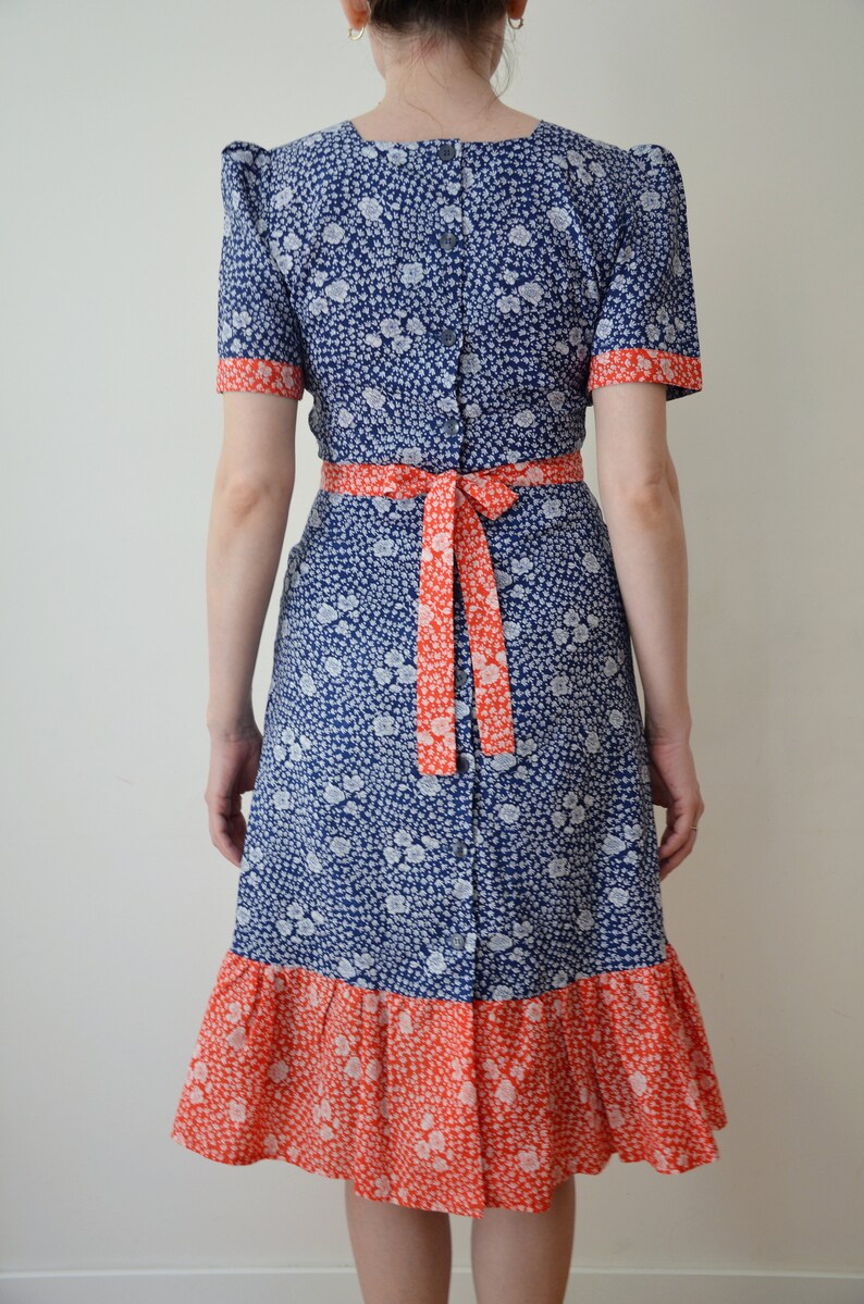 May include: A blue and red floral print dress with a ruffled hem and a tie at the waist.