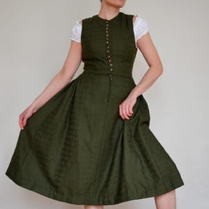 May include: A green dirndl dress with a white blouse and a button-up front. The dress has a full skirt and a fitted bodice.