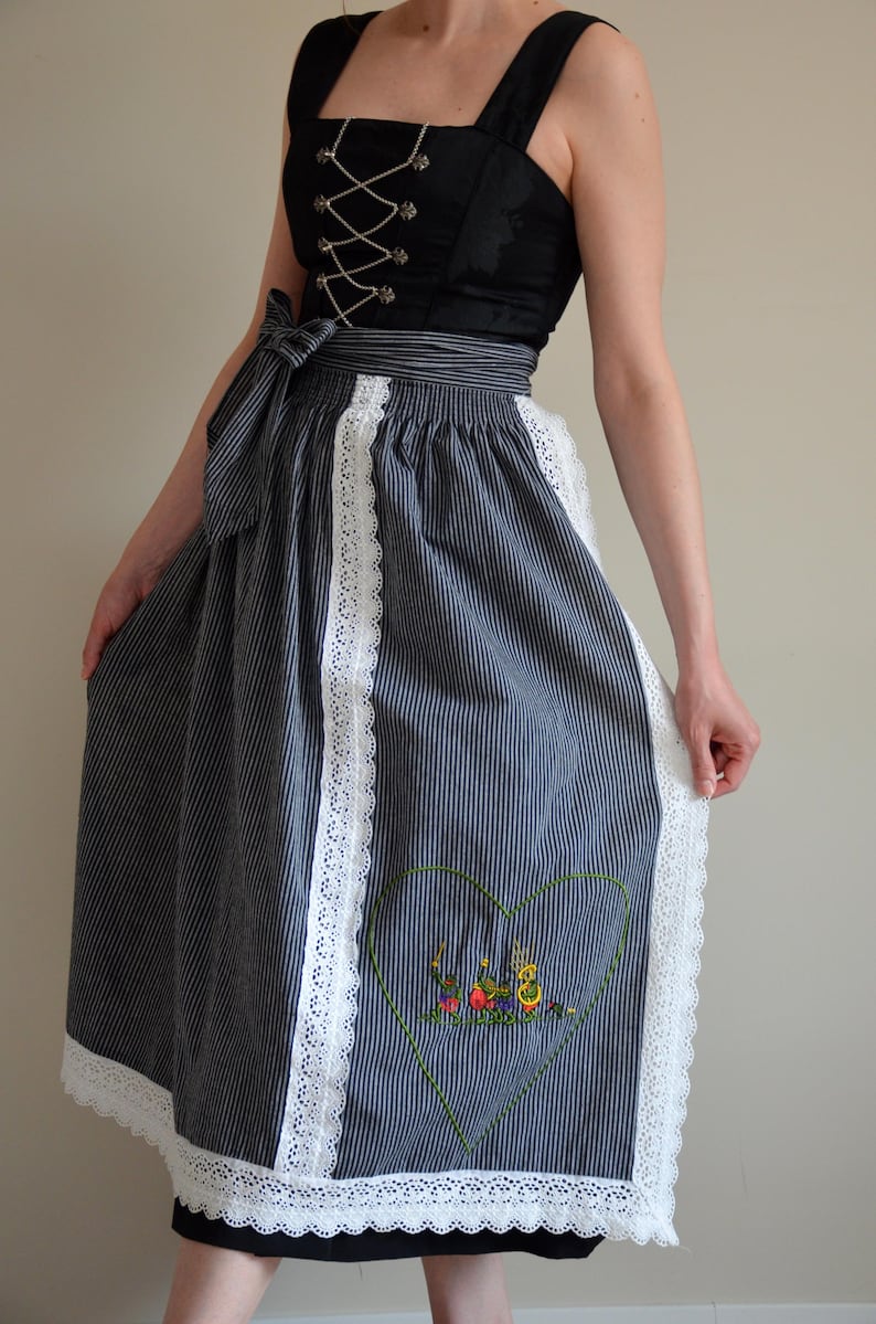 May include: A black and white striped dirndl skirt with white lace trim and an embroidered heart with a scene of people playing music.