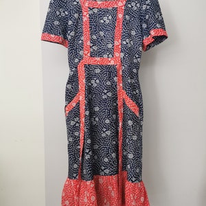 May include: A vintage blue and white floral dress with red trim. The dress has a square neckline, short sleeves, and a full skirt. It is a midi length dress.