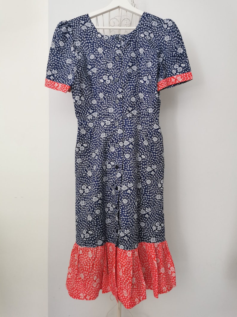 May include: A blue and white floral print dress with a red trim and a ruffled hem.