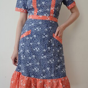 May include: A blue and white floral dress with a red trim. The dress has a square neckline, short sleeves, and a ruffled hem.