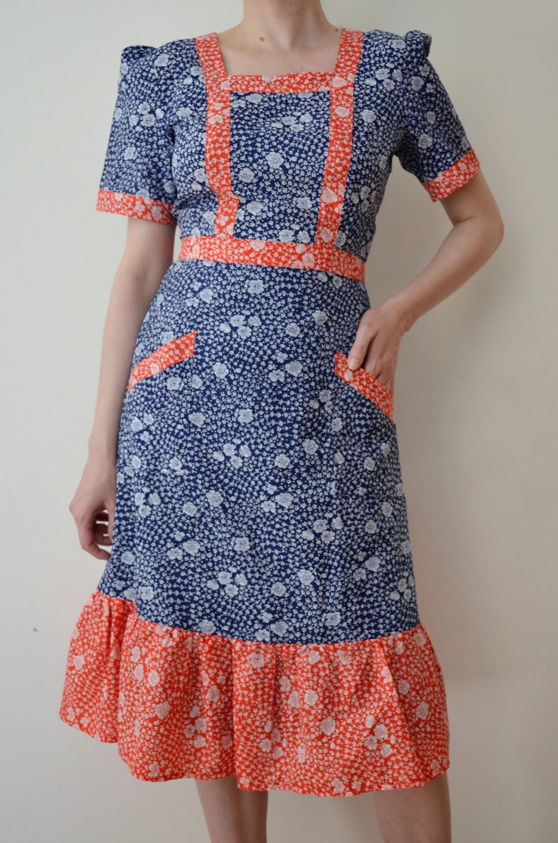 May include: A blue and white floral dress with a red trim. The dress has a square neckline, short sleeves, and a ruffled hem.