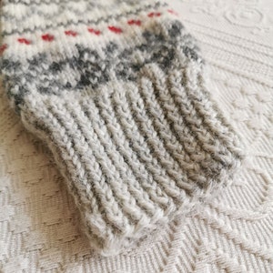 May include: Close-up of a gray and white knitted sweater cuff with a red and white patterned design.