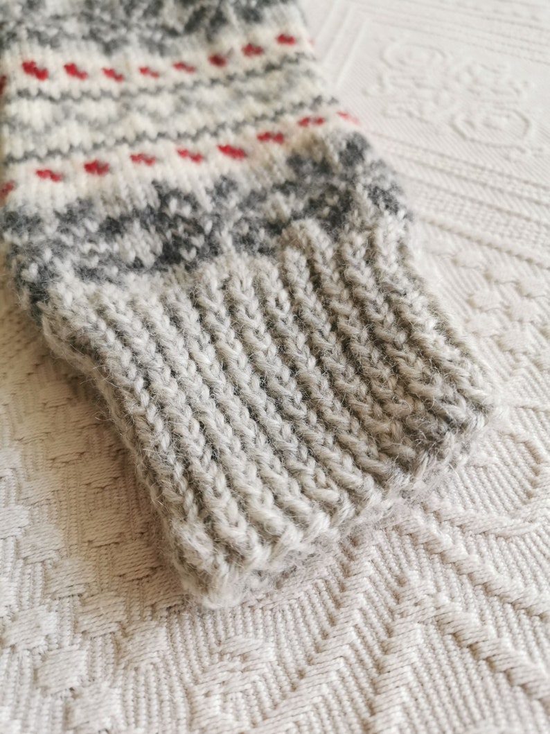 May include: Close-up of a gray and white knitted sweater cuff with a red and white patterned design.