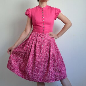 May include: A pink dress with a white floral print skirt and a solid pink bodice with a button-up front.