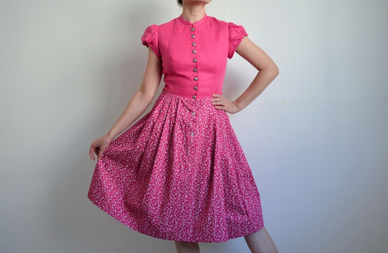 May include: A pink dress with a white floral print skirt and a solid pink bodice with a button-up front.